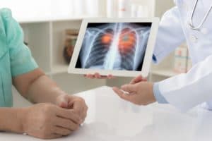 Doctor explaining results of lung check up from x-ray scan chest on digital tablet screen to patient.