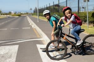 Pedestrians crossing along with their bicycle and skateboard.