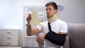 Injured man with cervical collar and arm sling reading medical bills.
