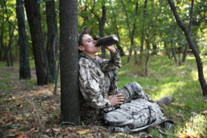 Soldier drinking water from canteen in the forest.
