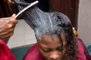 Hairdresser using hair relaxer to client.