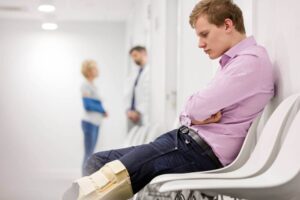 Man staring at brace on knee while sitting in hospital waiting room.
