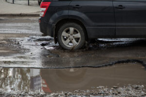 Car tire about to pass through large pothole of water.