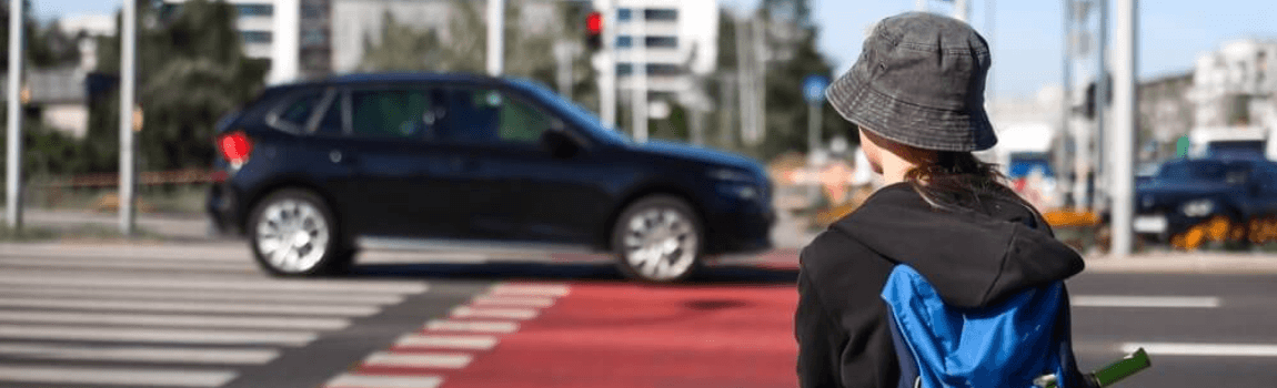 School-age teenage boy with bike waiting at pedestrian crosswalk.