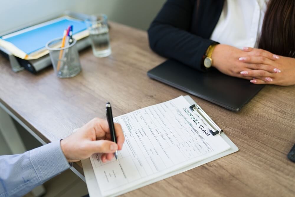 Client's hand filling out an insurance claim form.